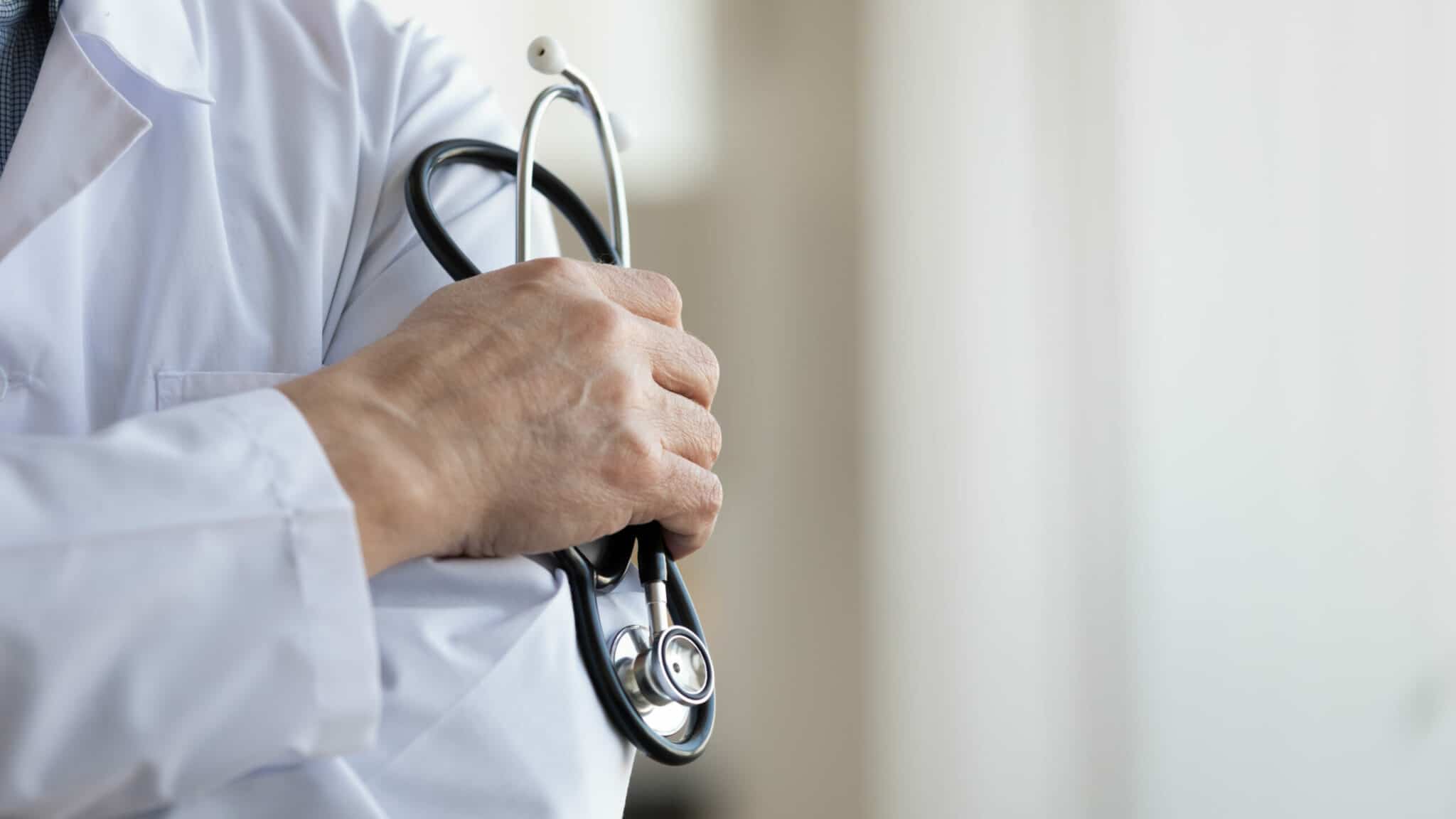 Médecin généraliste masculin et professionnel portant un uniforme blanc tenant un stéthoscope à la main. Vue en gros plan.